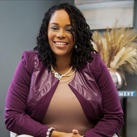 The woman is wearing a purple jacket and smiling for the camera.
