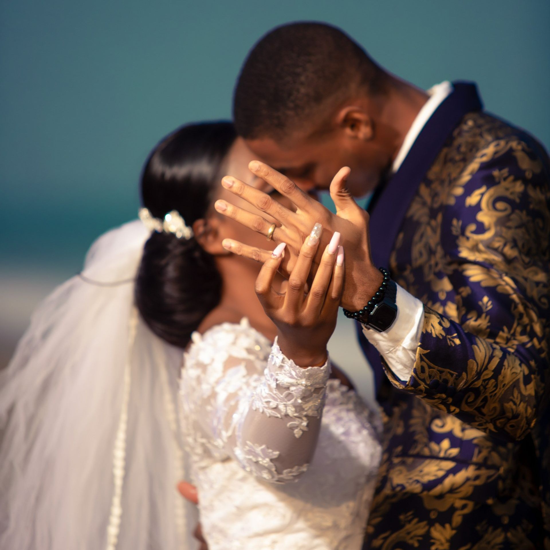 A bride and groom kissing on the beach with the bride wearing a wedding ring