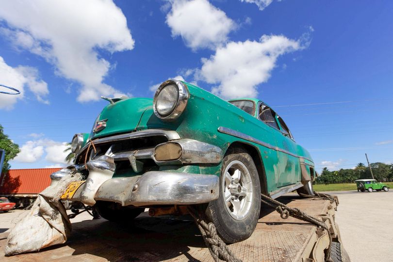 Teal vintage car wreck on a tow truck under a bright blue sky