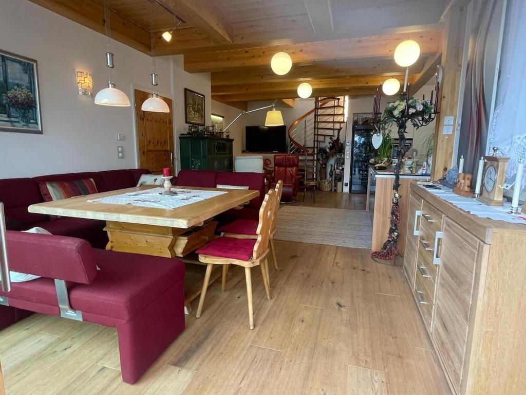 Gemütliches Esszimmer mit roten Stühlen, Holztisch, Pendelleuchten und einer Treppe im hinteren Bereich.