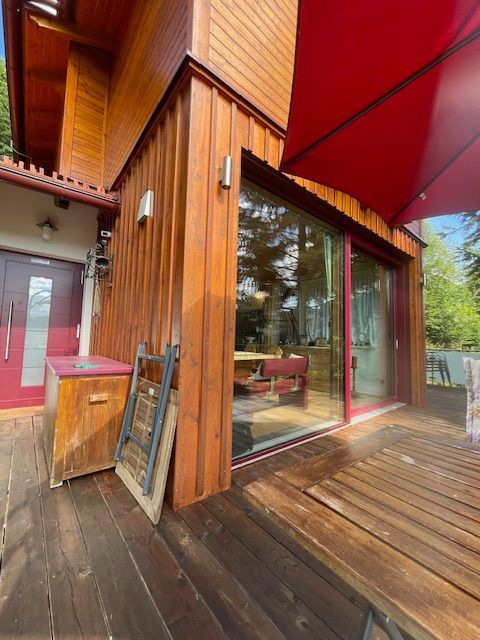 Holzterrasse im Außenbereich mit großen Glasfenstern und roter Markise an einem regnerischen Tag