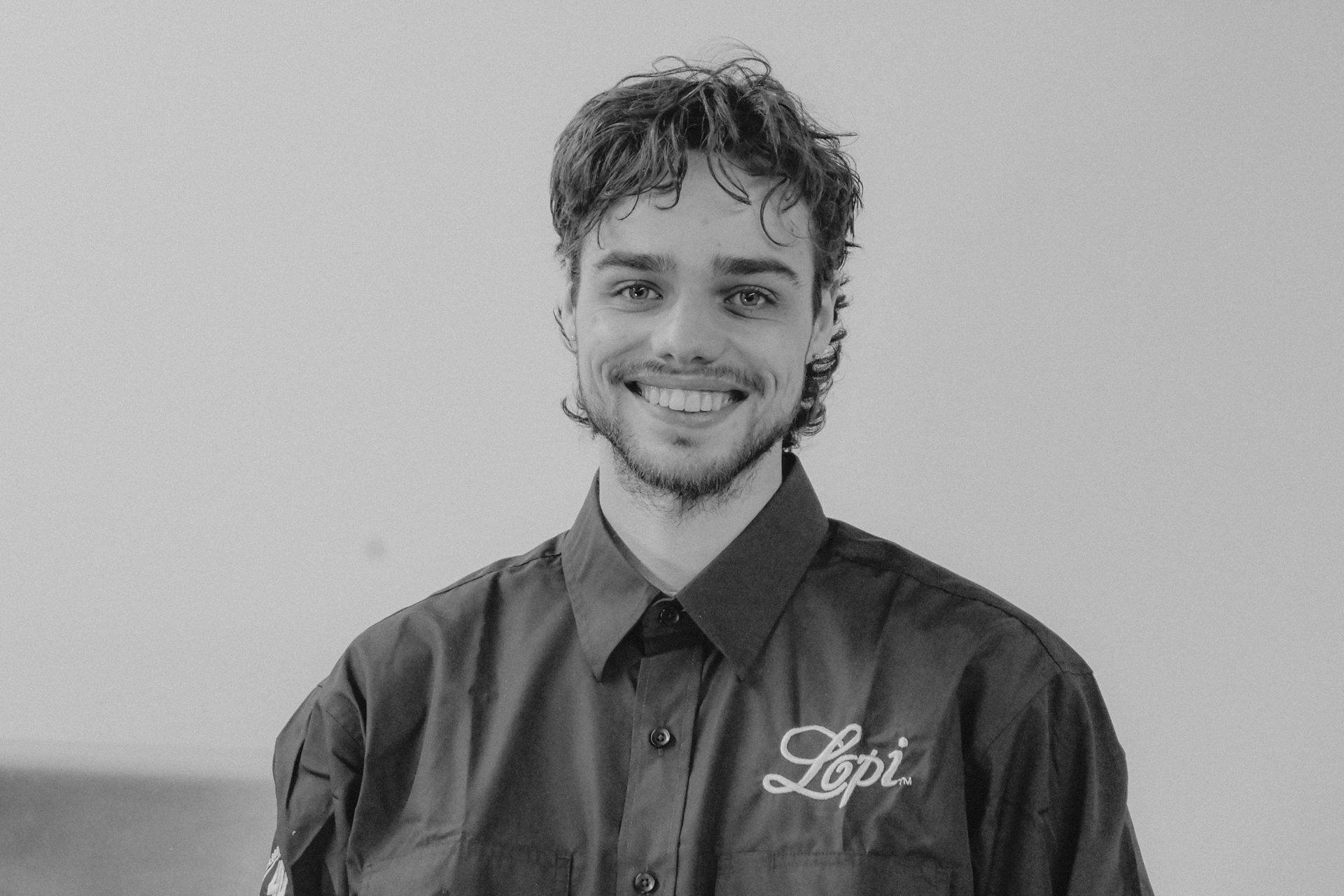 Man with curly hair, smiling, wearing a dark button-up shirt with