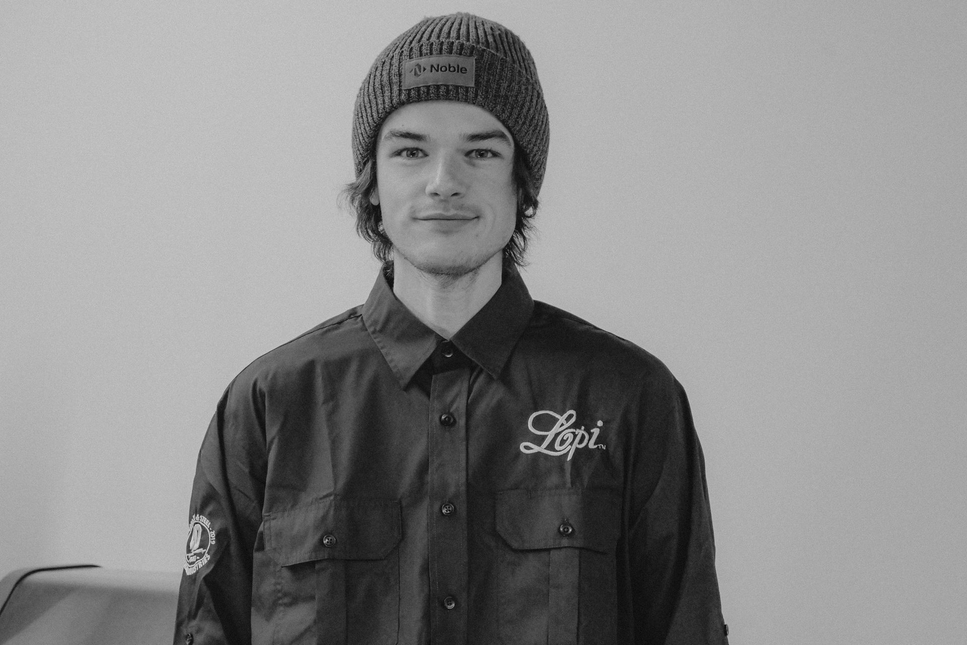 Man in a beanie and button-up shirt smiling at the camera, indoors.