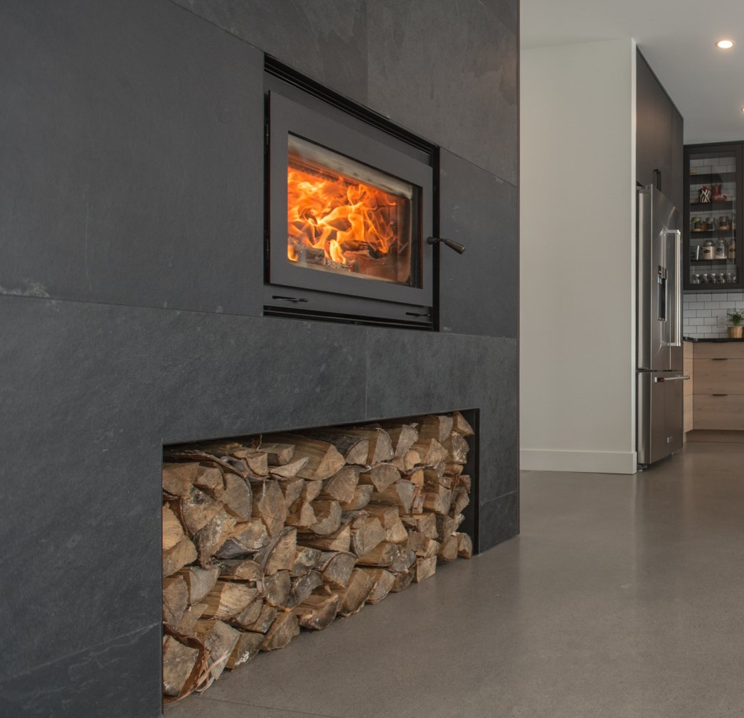Fireplace with burning flames and wood storage below, dark stone wall.