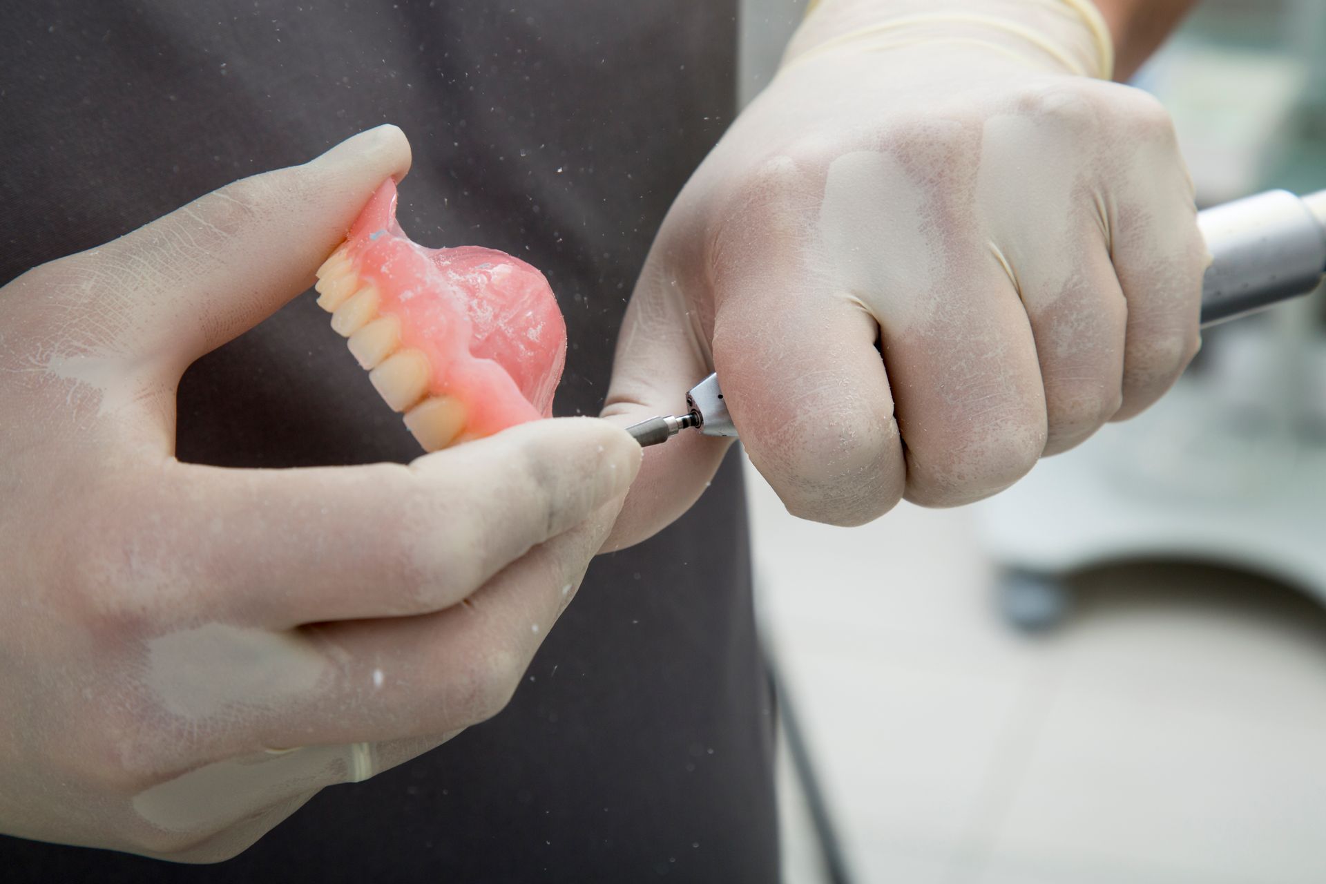 A dentist is grinding a denture with a grinder