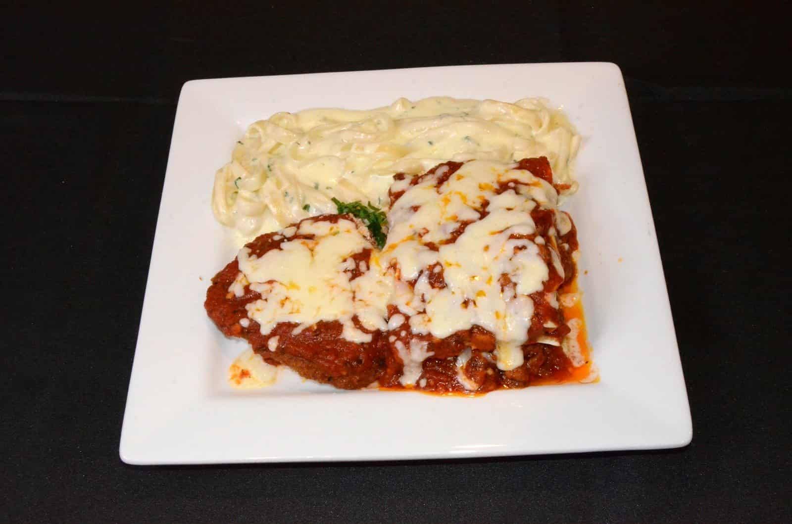 Chicken Parmesan with mashed potatoes on a white plate, dark background.