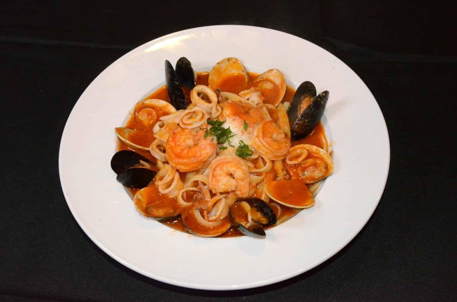 Plate of seafood pasta with shrimp, mussels, calamari, and scallops in tomato sauce.