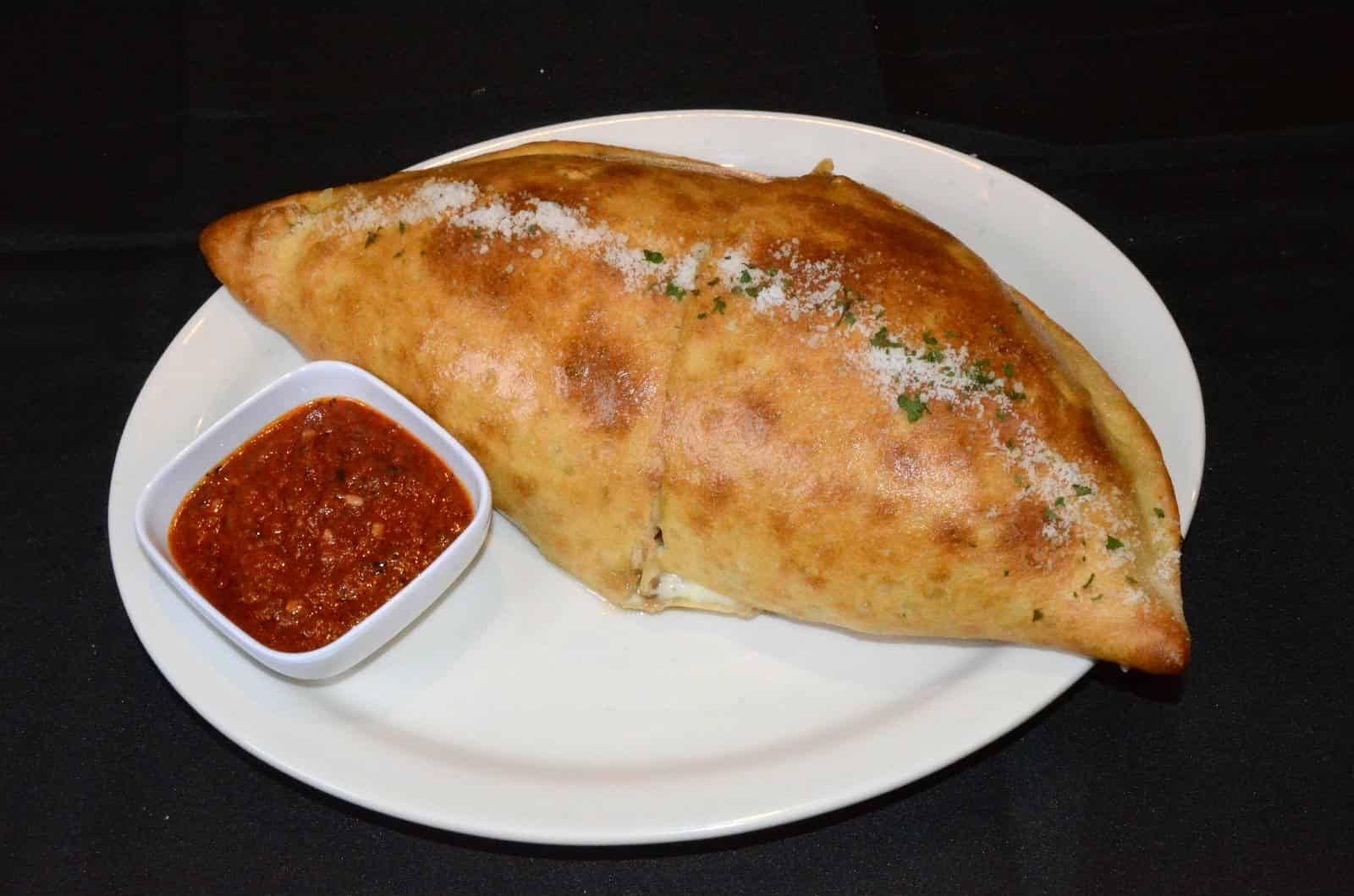 Calzone on a plate with marinara dipping sauce.