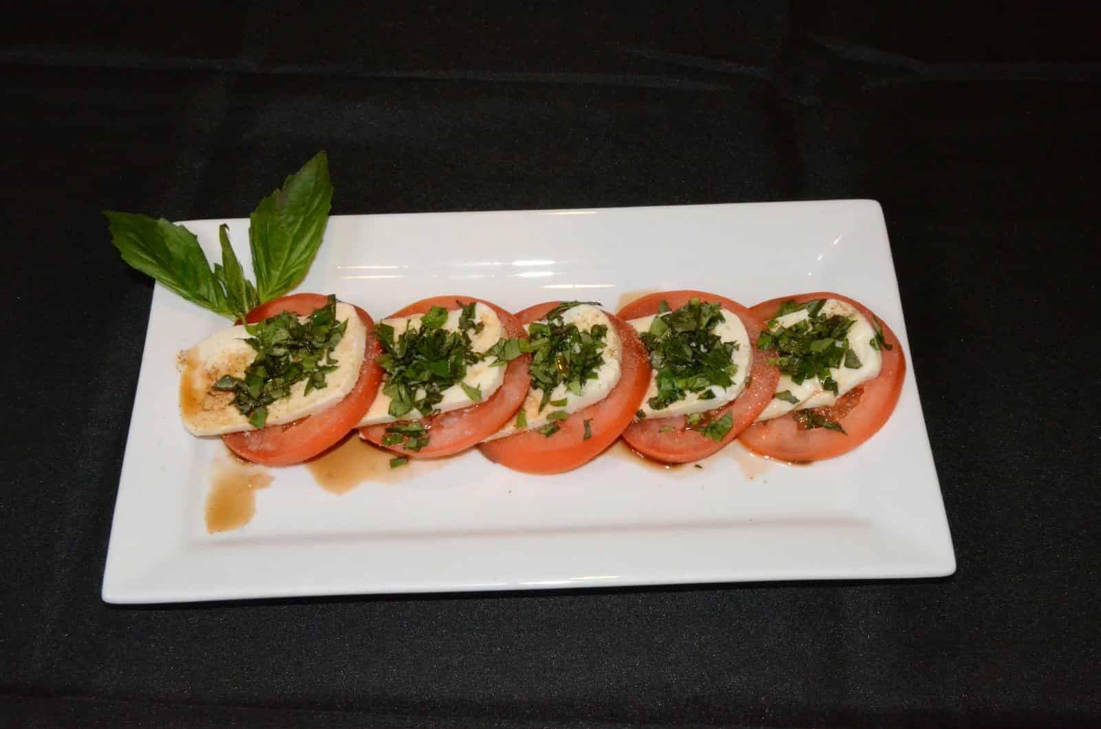 Sliced tomatoes and mozzarella with basil on a white rectangular plate.