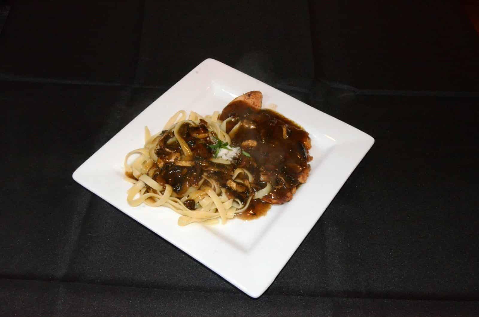 Steak with gravy and noodles on a white square plate, black background.