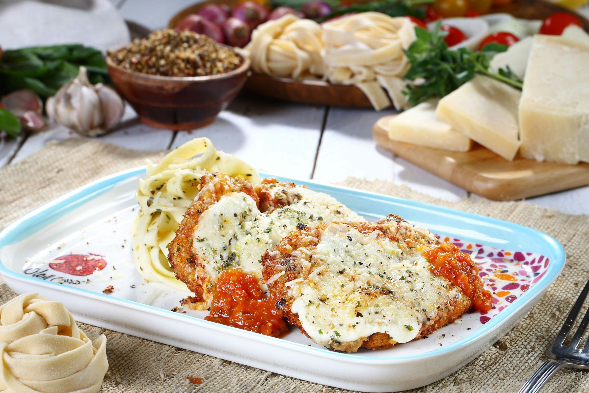 Chicken Parmesan with pasta on a rectangular plate, ingredients in background.