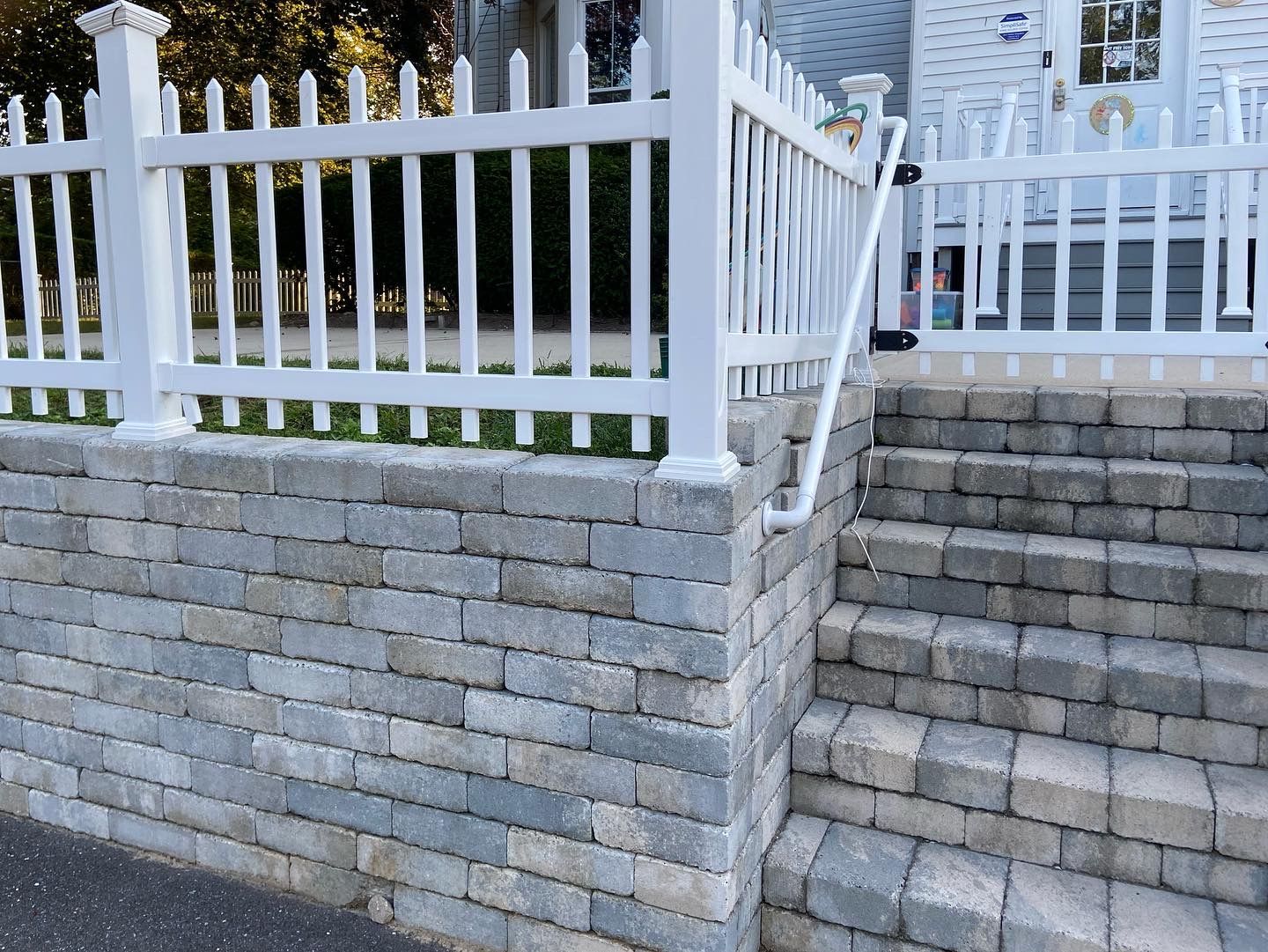 A white picket fence surrounds a stone wall and stairs