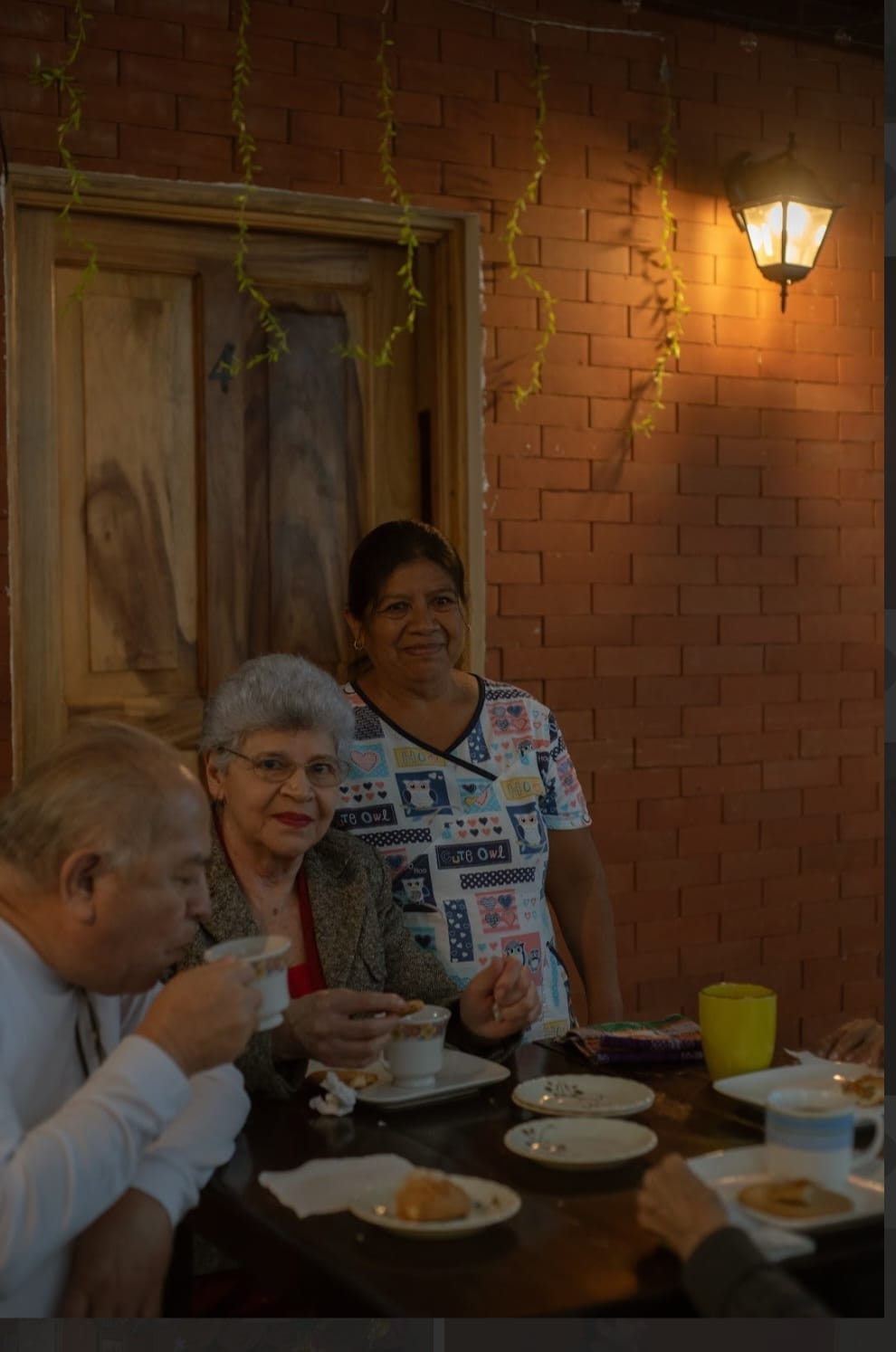 Personas cenando juntas en una mesa de patio de ladrillo cálidamente iluminada por la noche.