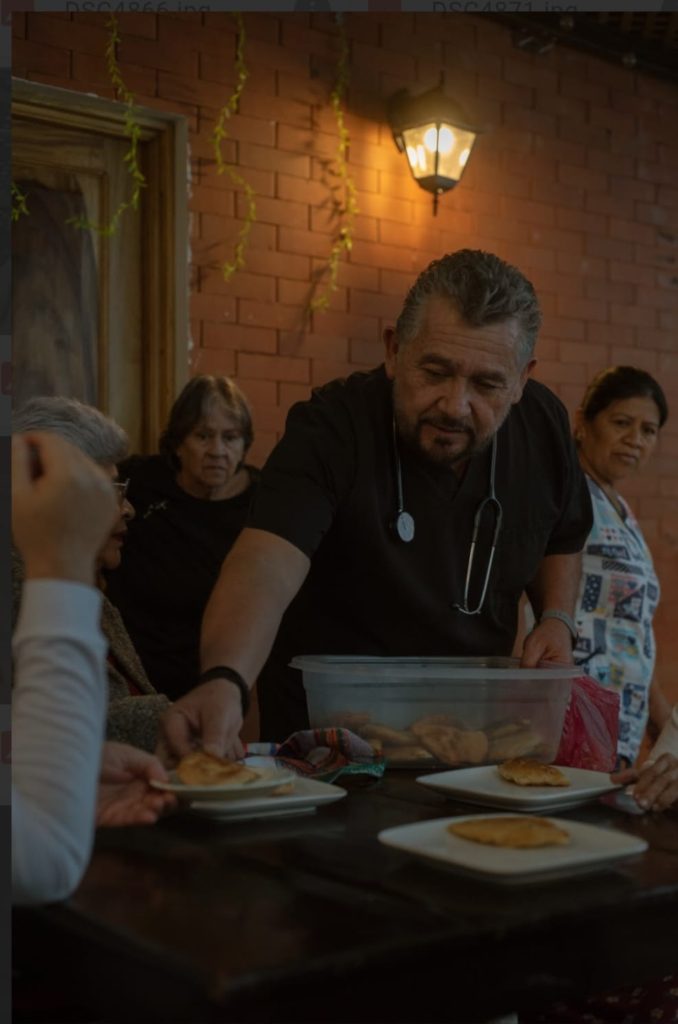 Un hombre sirve comida en una mesa en una habitación con paredes de ladrillo cálidamente iluminada.