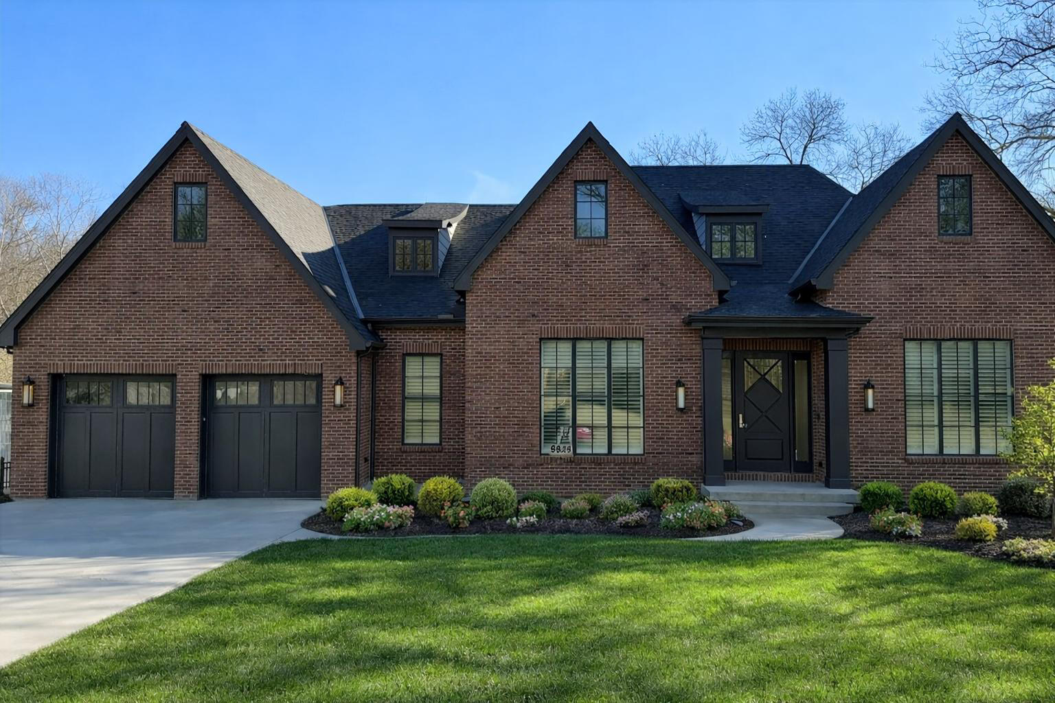 Brick suburban house with two garages, gabled roof, and manicured front lawn