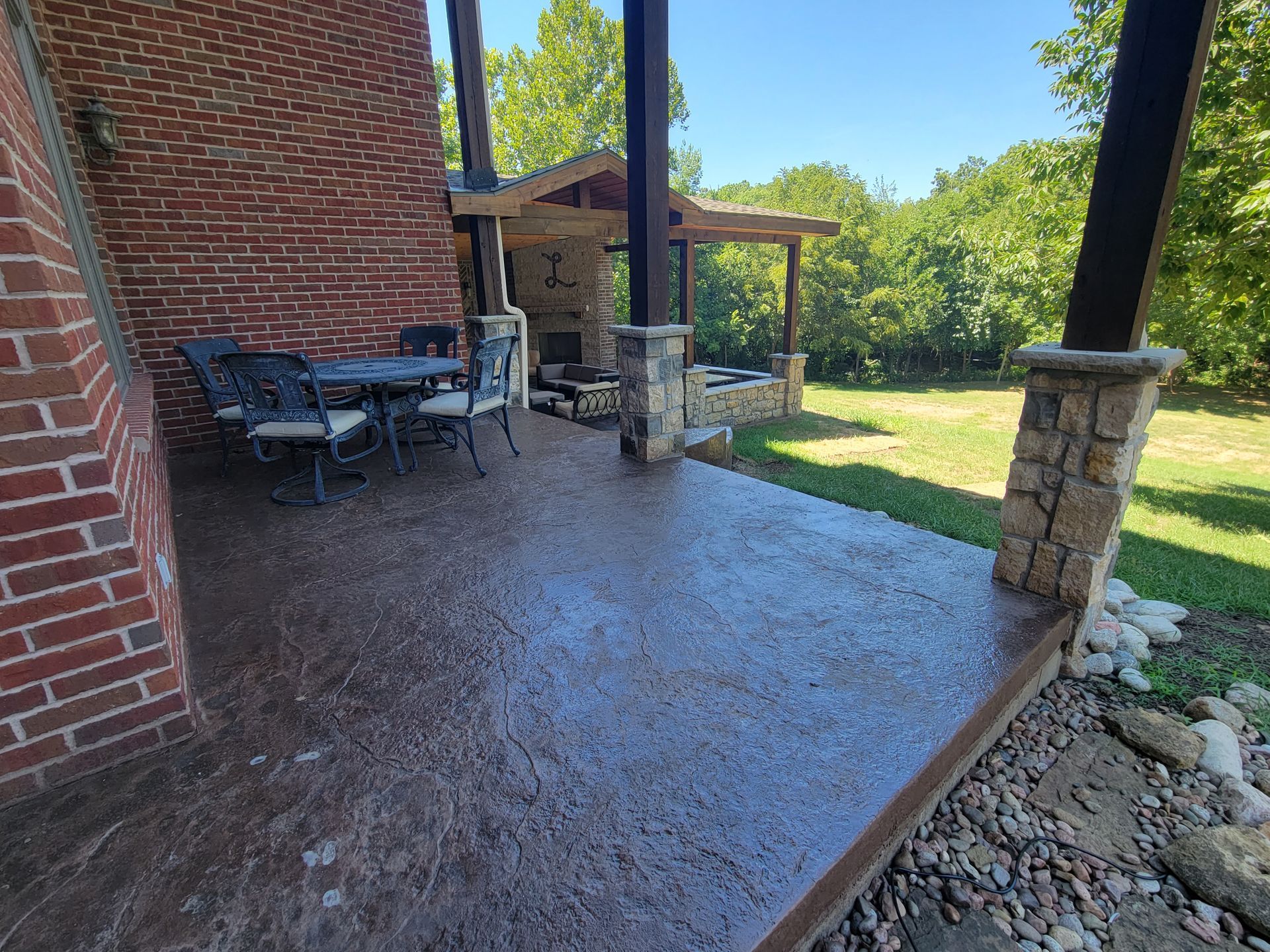 Covered brick patio with stone columns, outdoor table and chairs, and a grassy yard beyond.