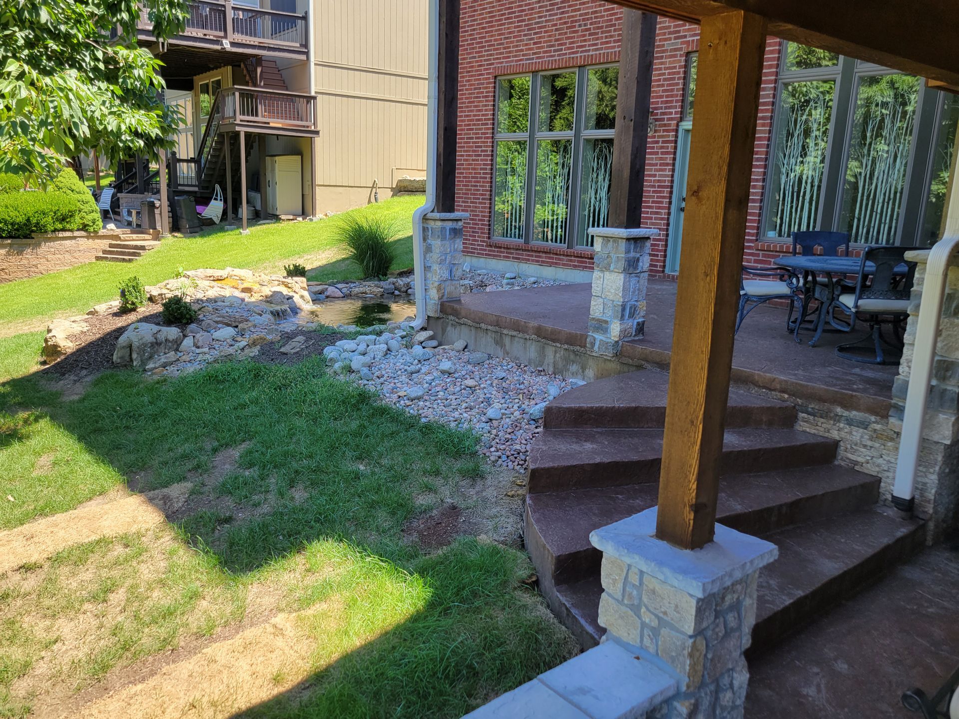 Backyard patio with brick house, steps, wooden post, and grassy lawn beside a gravel border