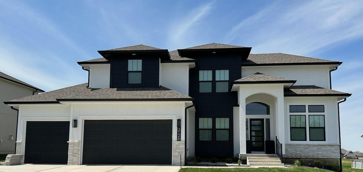 Modern two-story house with dark garage doors, white exterior, and black accents under a blue sky