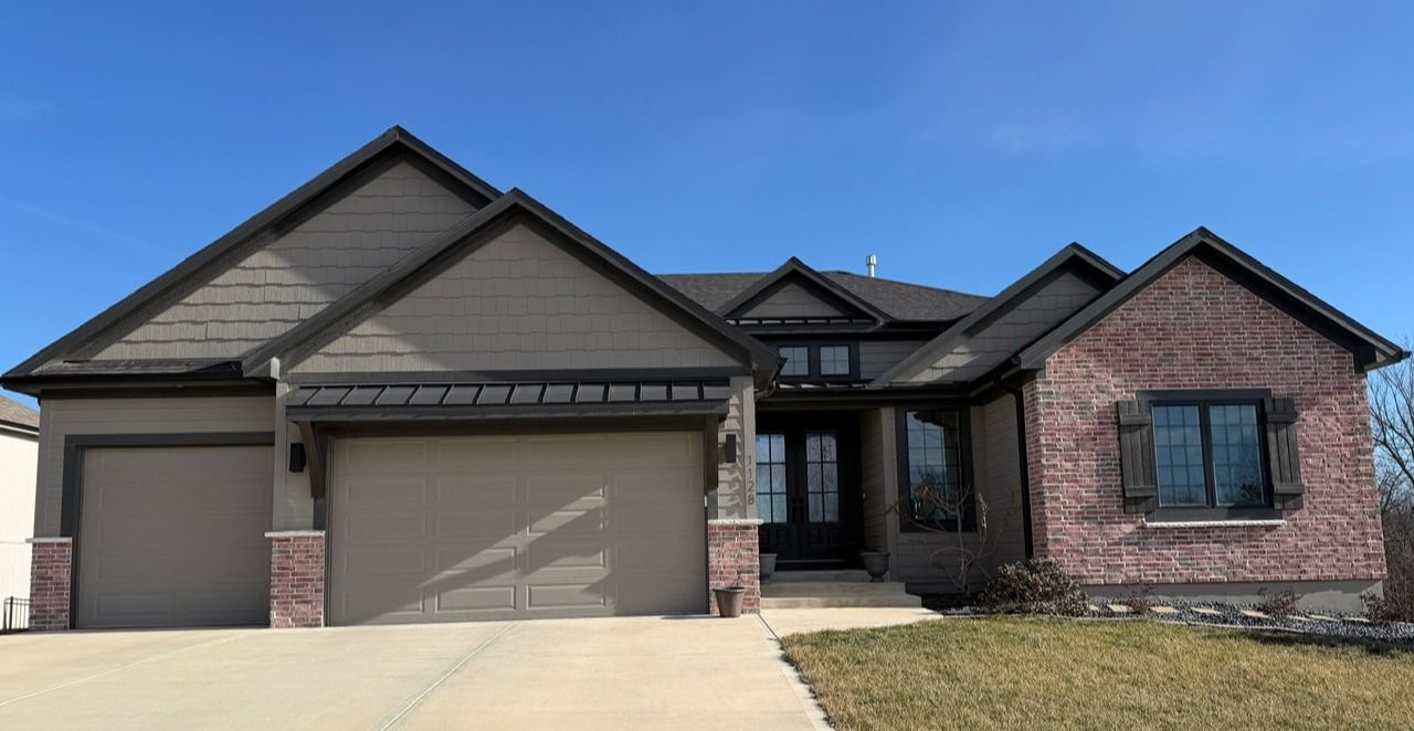 Single-story suburban brick house with a two-car garage and concrete driveway under a clear blue sky