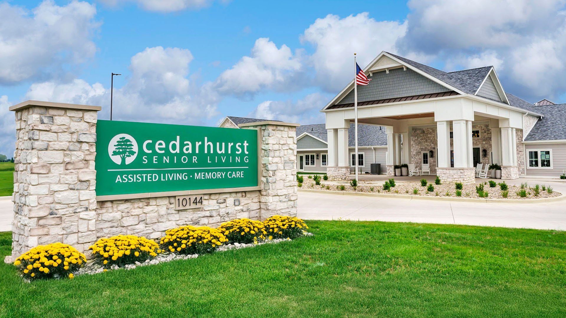 Cedarhurst senior living entrance with green sign, stone pillar, white building, and landscaped lawn