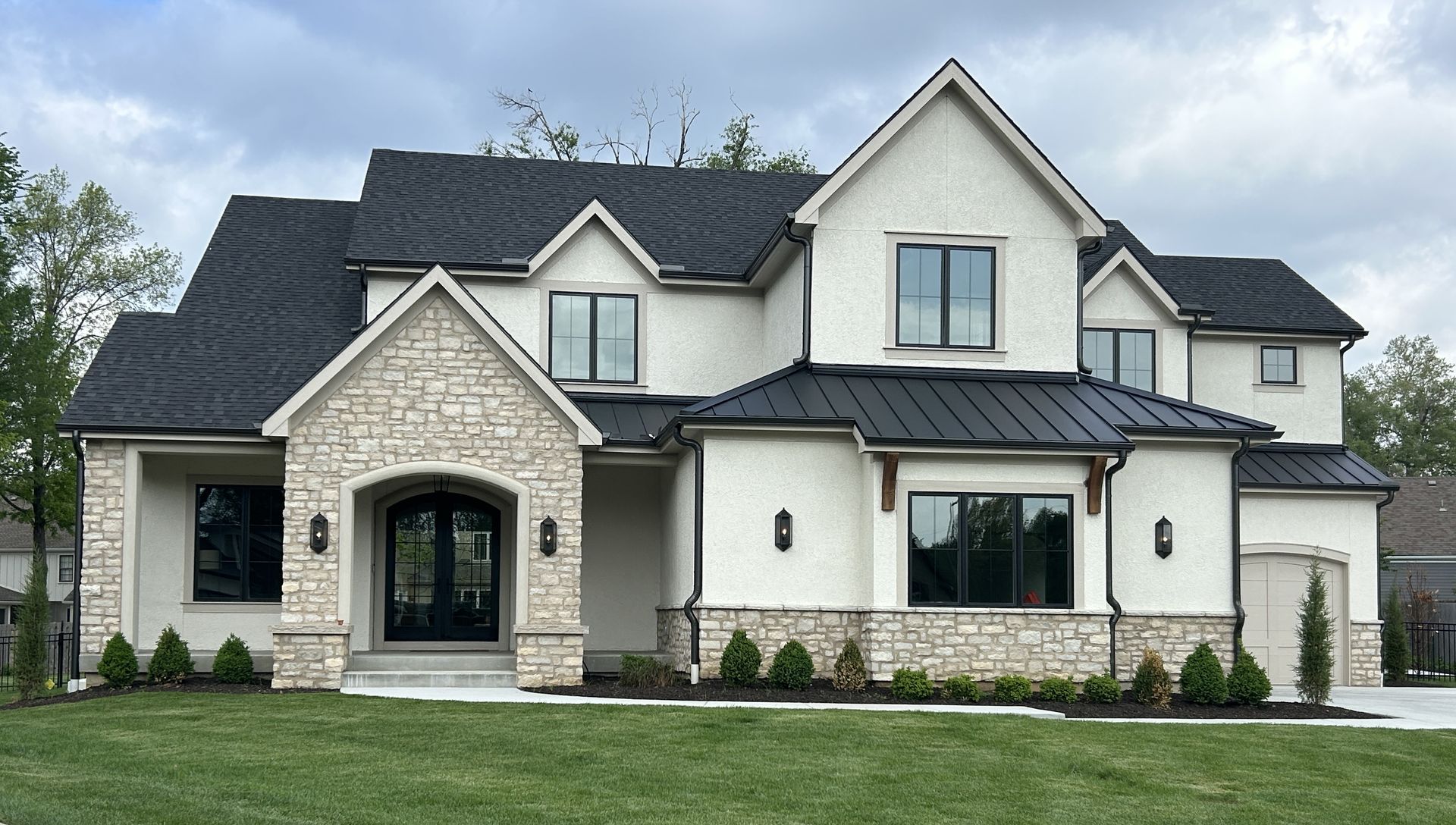 Large modern two-story house with stone facade, dark roof, and manicured lawn