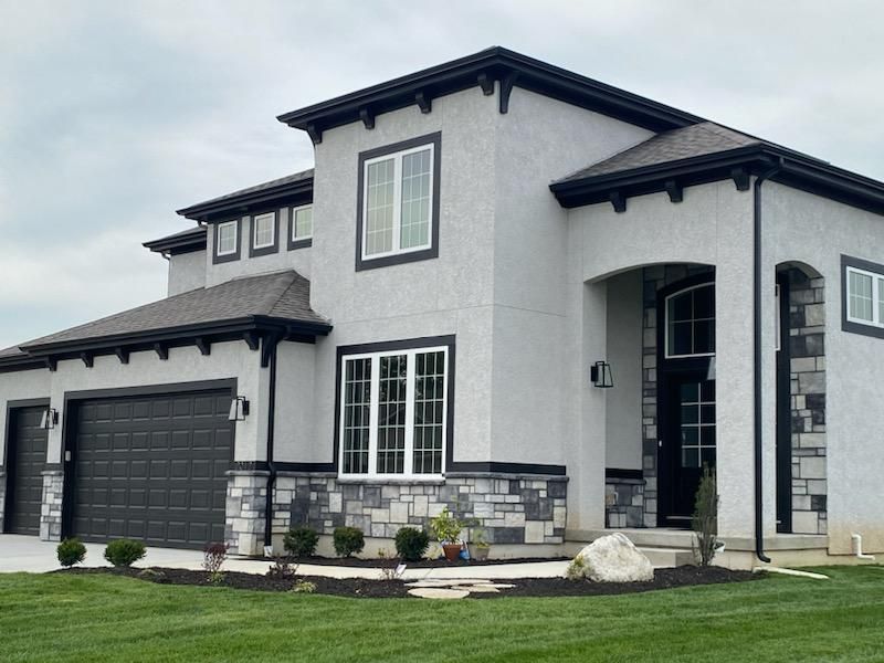 Modern two-story gray house with black trim, garage, arched entryway, and landscaped front yard