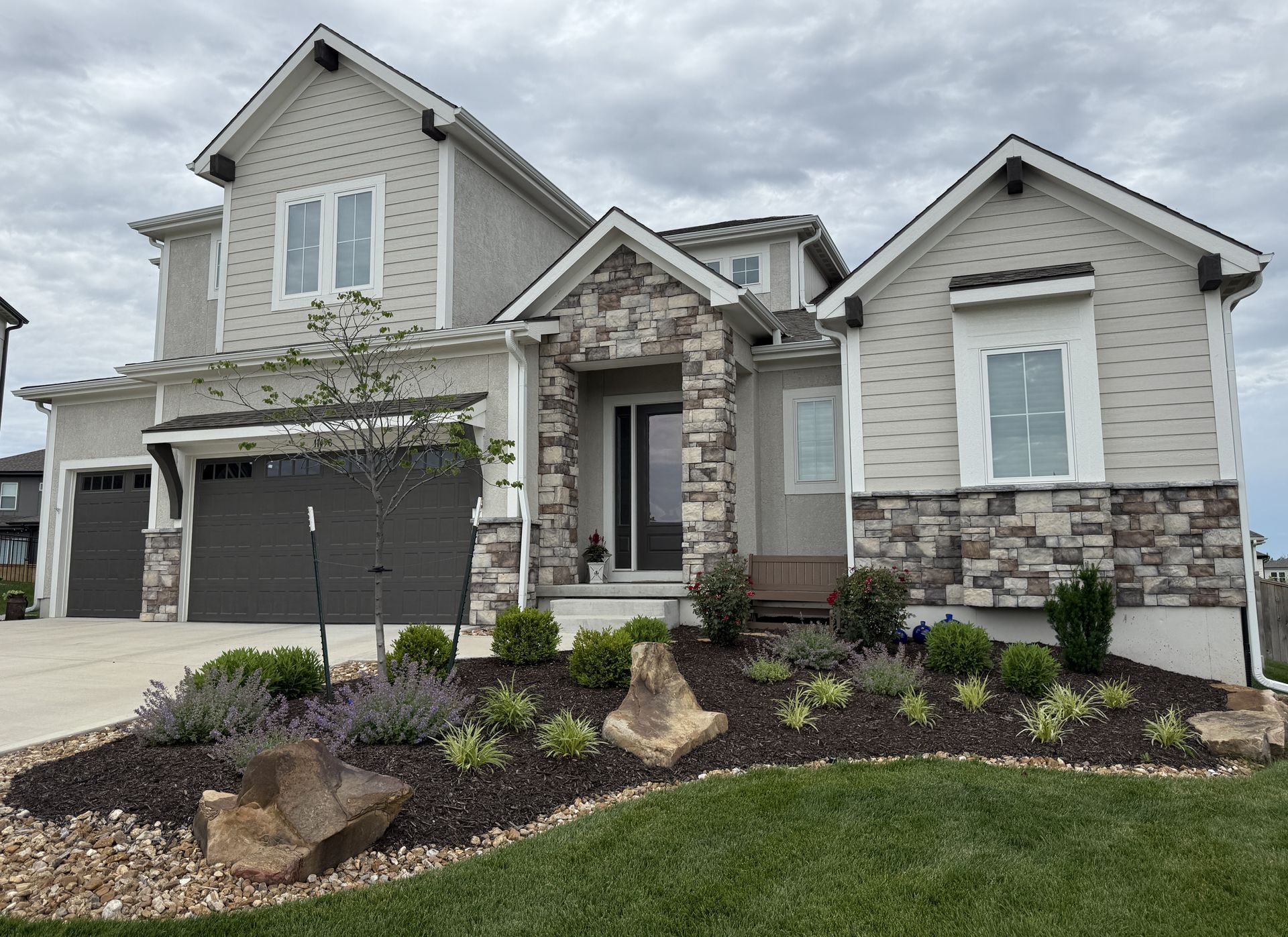 Modern two-story gray stone-and-siding house with a front porch, garage, and landscaped flower bed