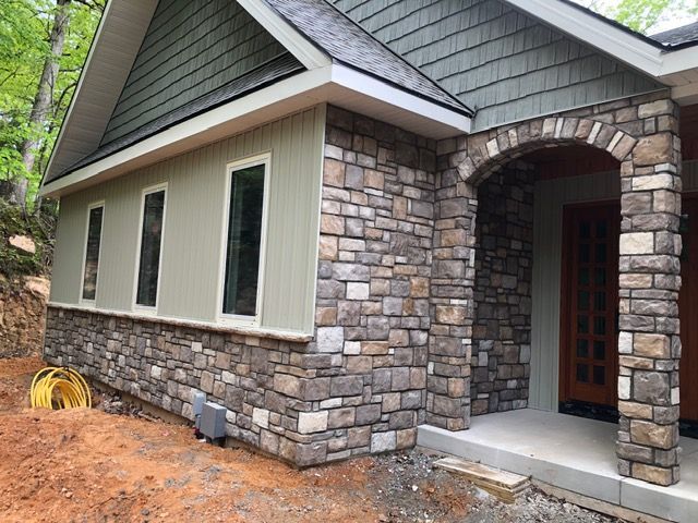 Stone house exterior with arched porch, beige siding, and white-trimmed windows amid dirt landscaping