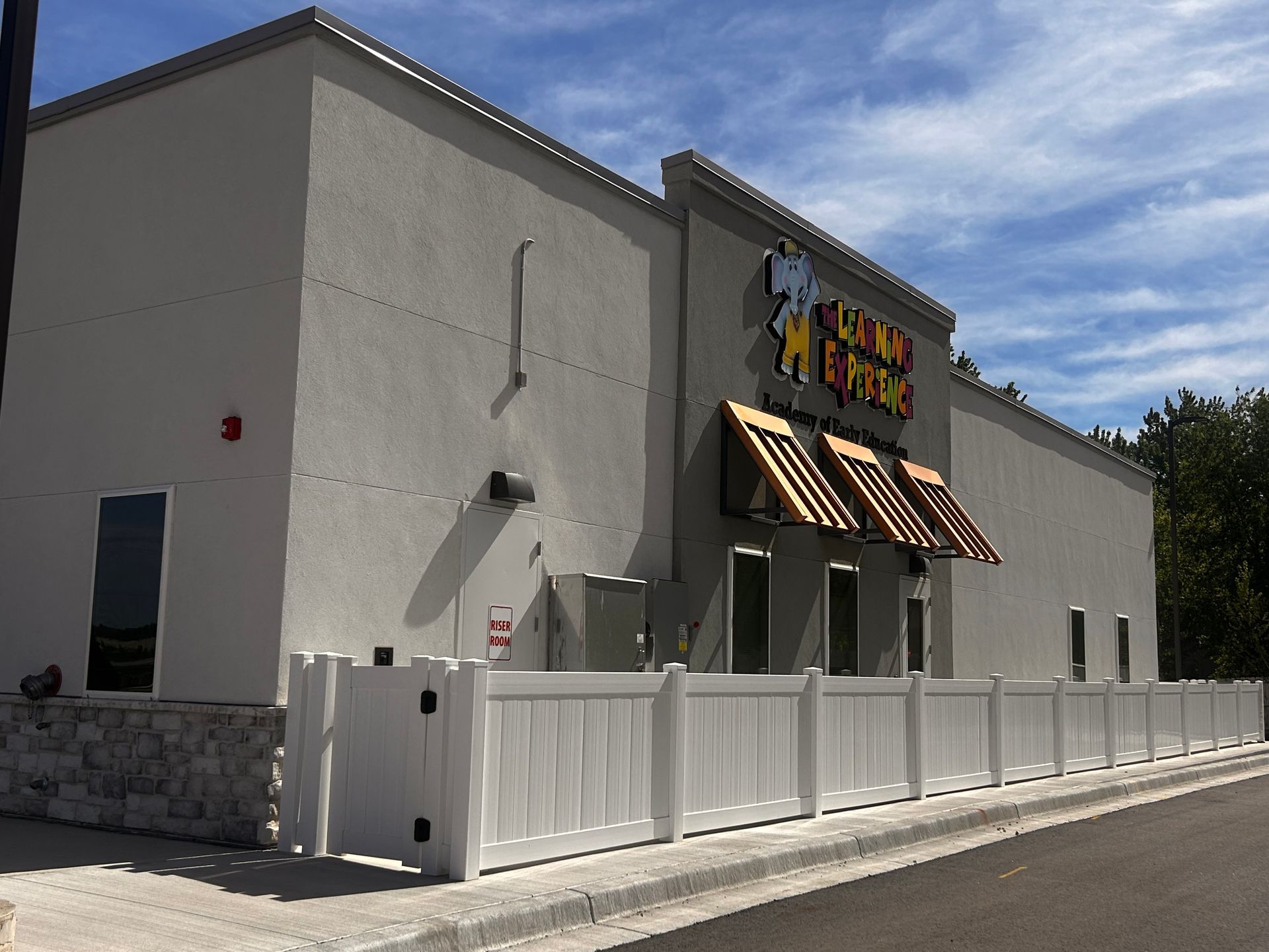 White storefront with striped awning, fenced patio, and large sign under a blue sky.