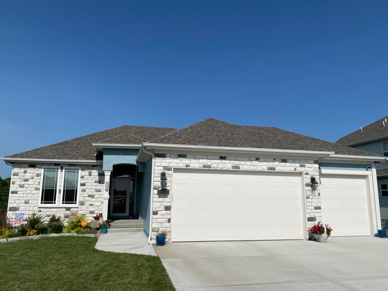 Suburban house with stone facade, two white garage doors, and a clear blue sky