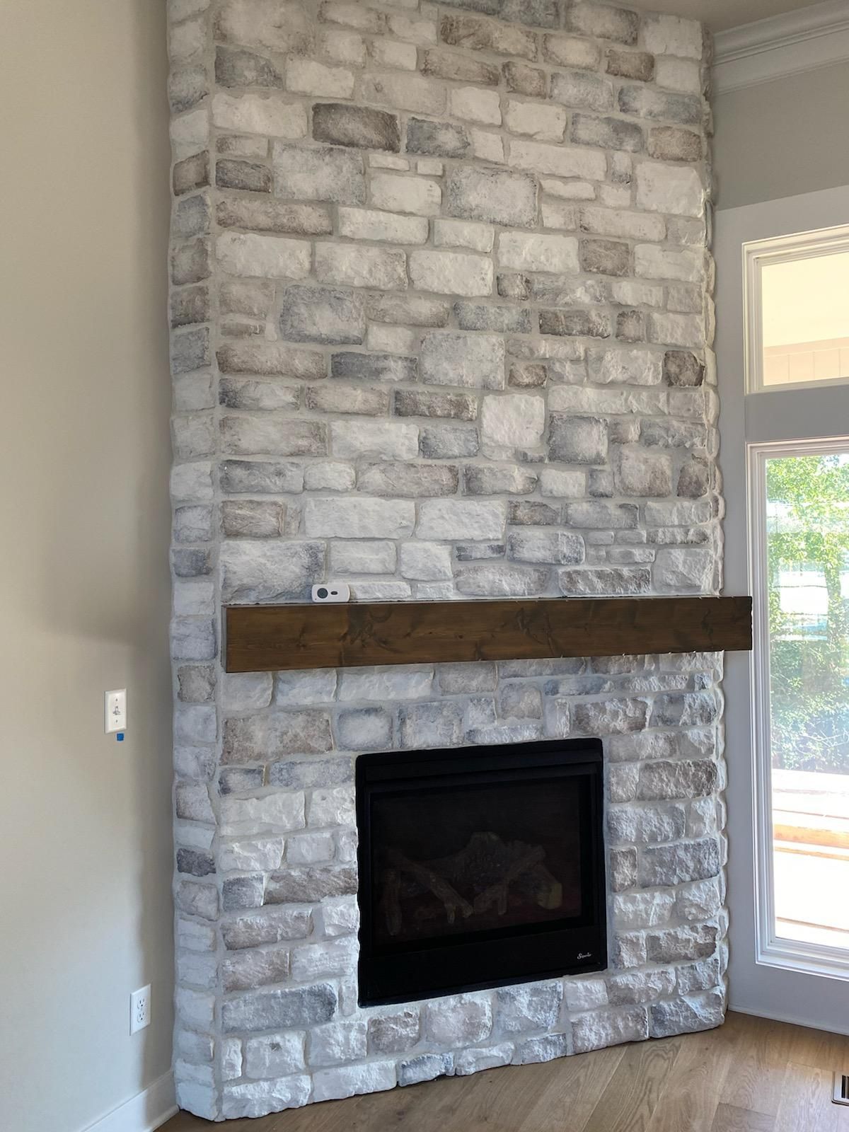 Stone fireplace with dark wood mantel and black firebox in a bright room
