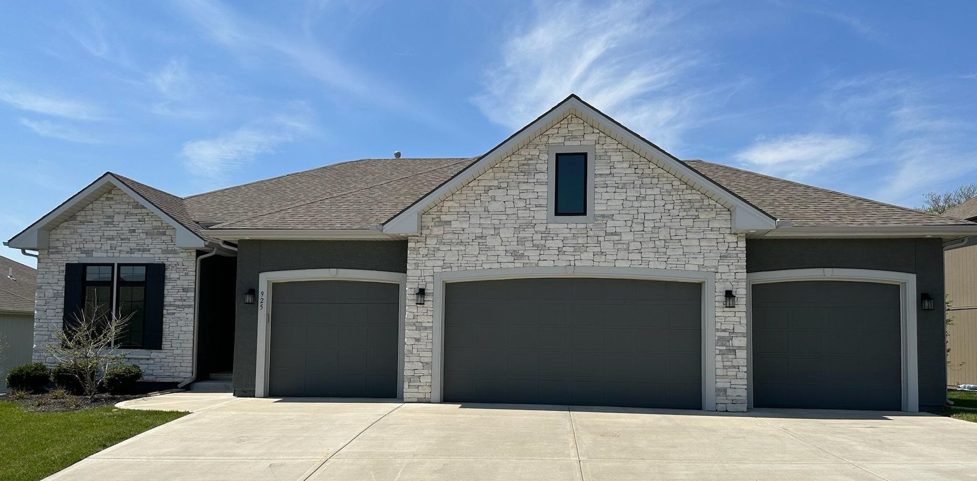 Single-story stone house with three garages and a dark roof under a blue sky.