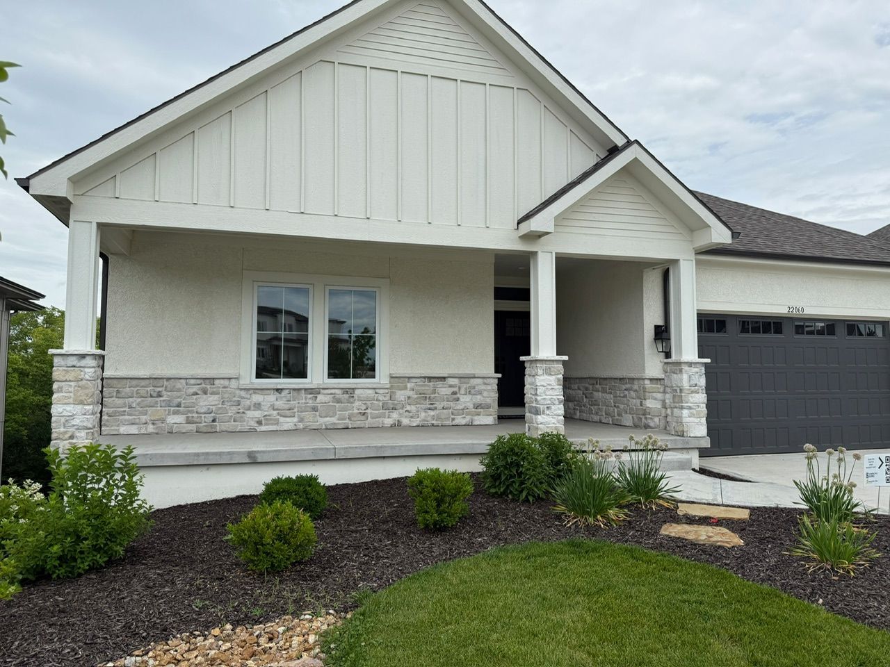 Modern white suburban house with stone accents, dark garage door, and landscaped front yard