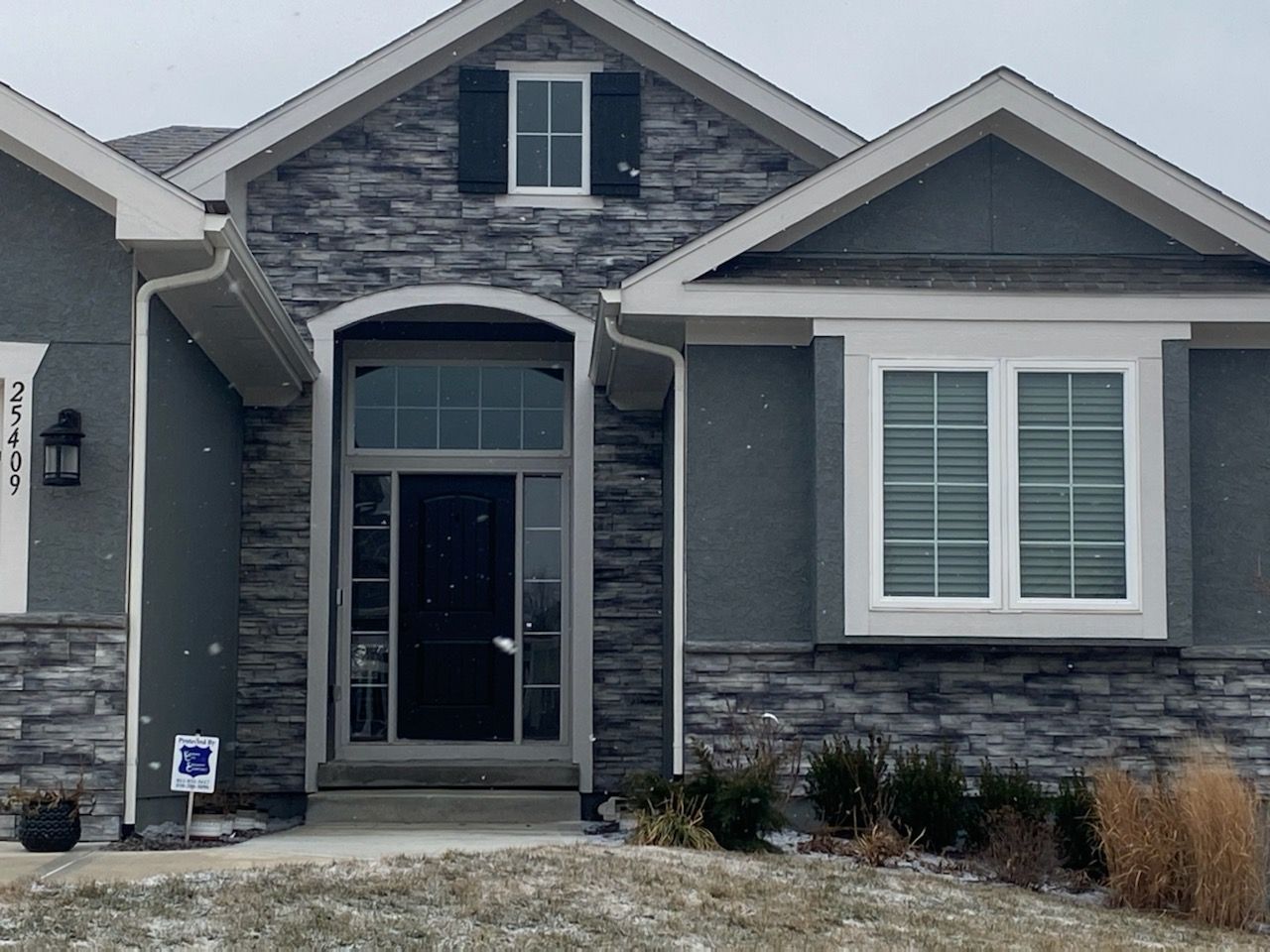 Front view of a gray stone house with a covered entry and white-trimmed windows.