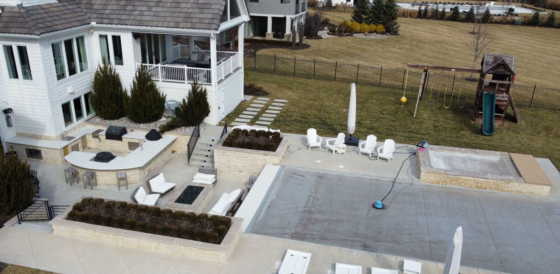 Backyard patio with white house, outdoor furniture, fire pit, and hot tub near a fenced lawn