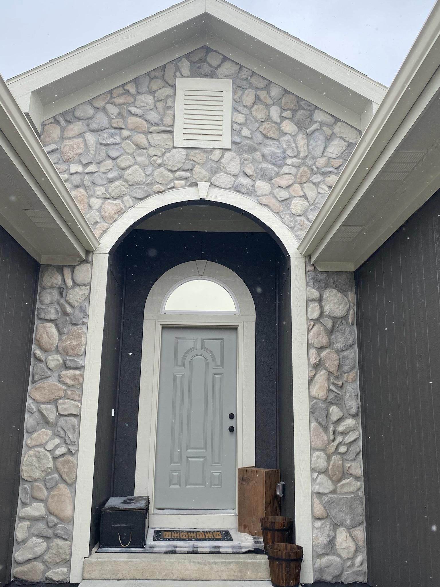 Stone-front house entry with gray door, arched porch, and black mailbox on the steps