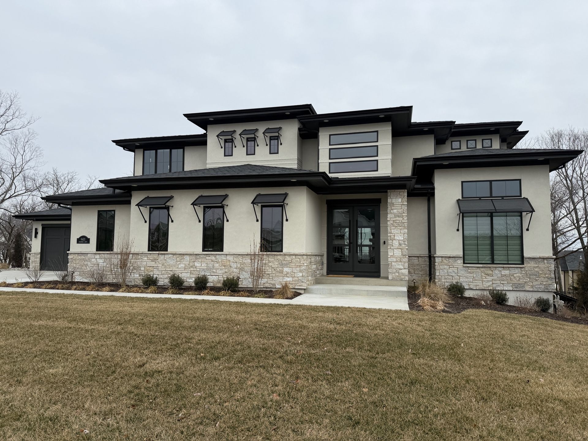 Modern two-story beige house with dark trim and a front lawn under an overcast sky