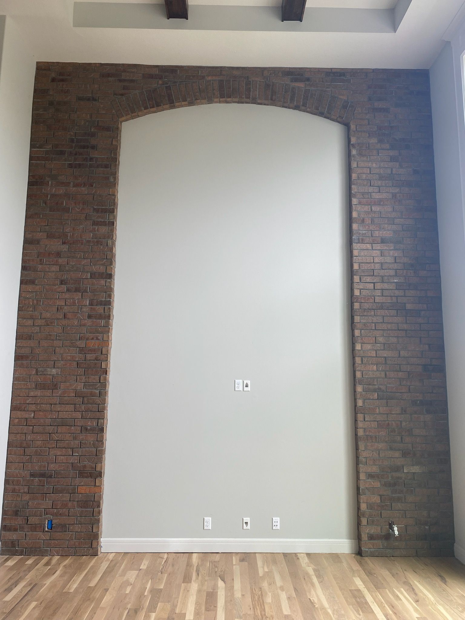 Empty brick-framed wall with a large arched white inset in an unfinished interior room