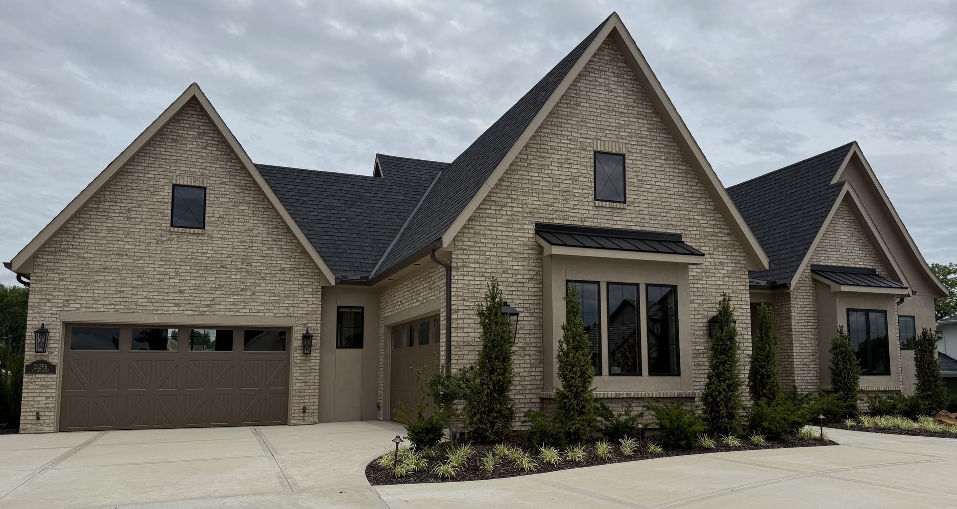 Stone suburban house with gabled roof, tan garage, and front windows under a cloudy sky