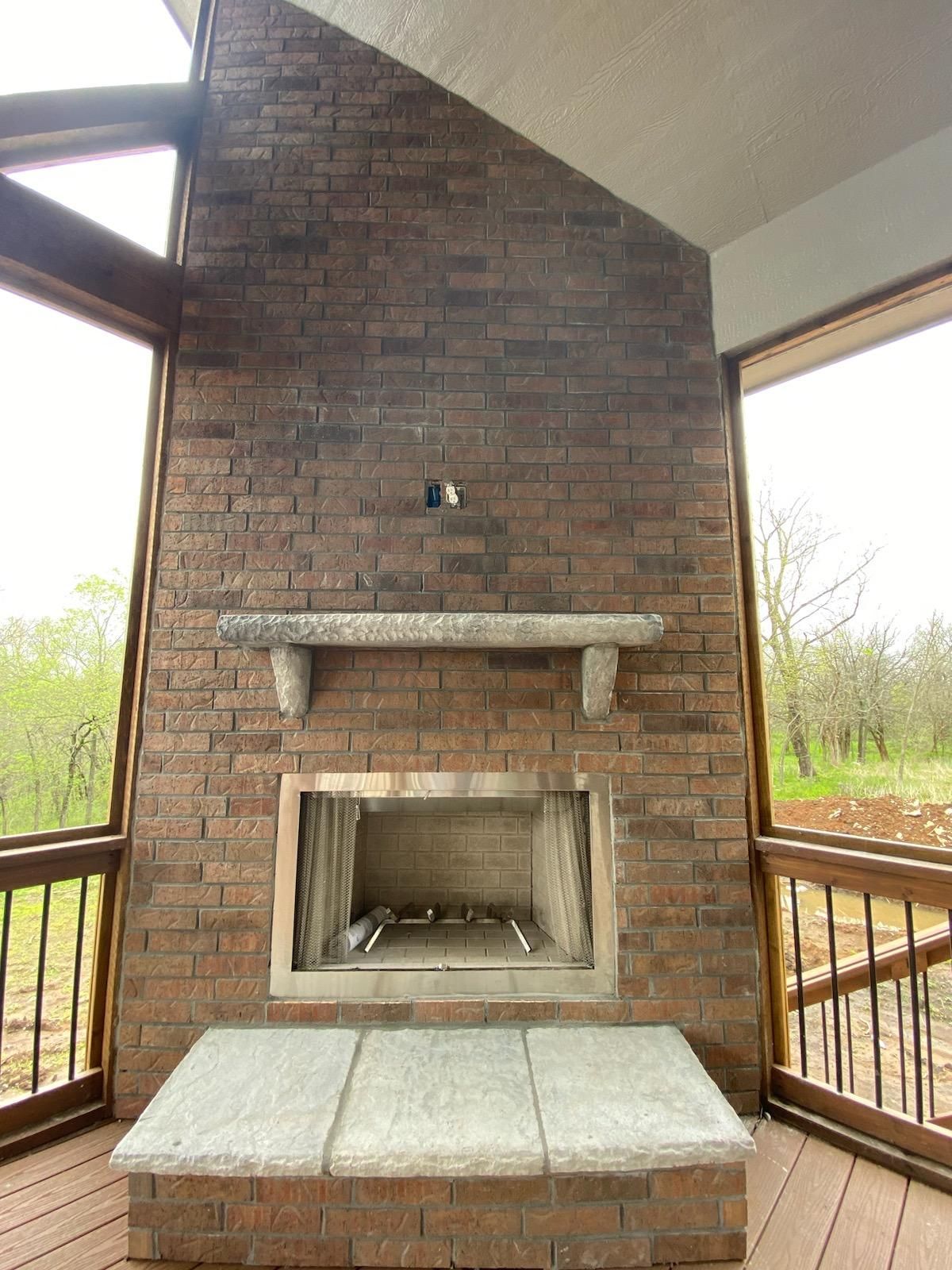 Brick outdoor fireplace with stone hearth on a covered porch overlooking trees