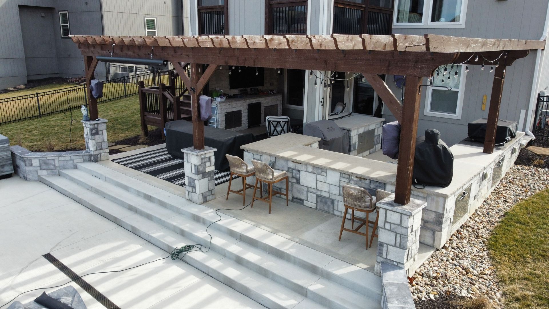 Backyard patio with white steps, pergola, outdoor dining table, and covered seating area