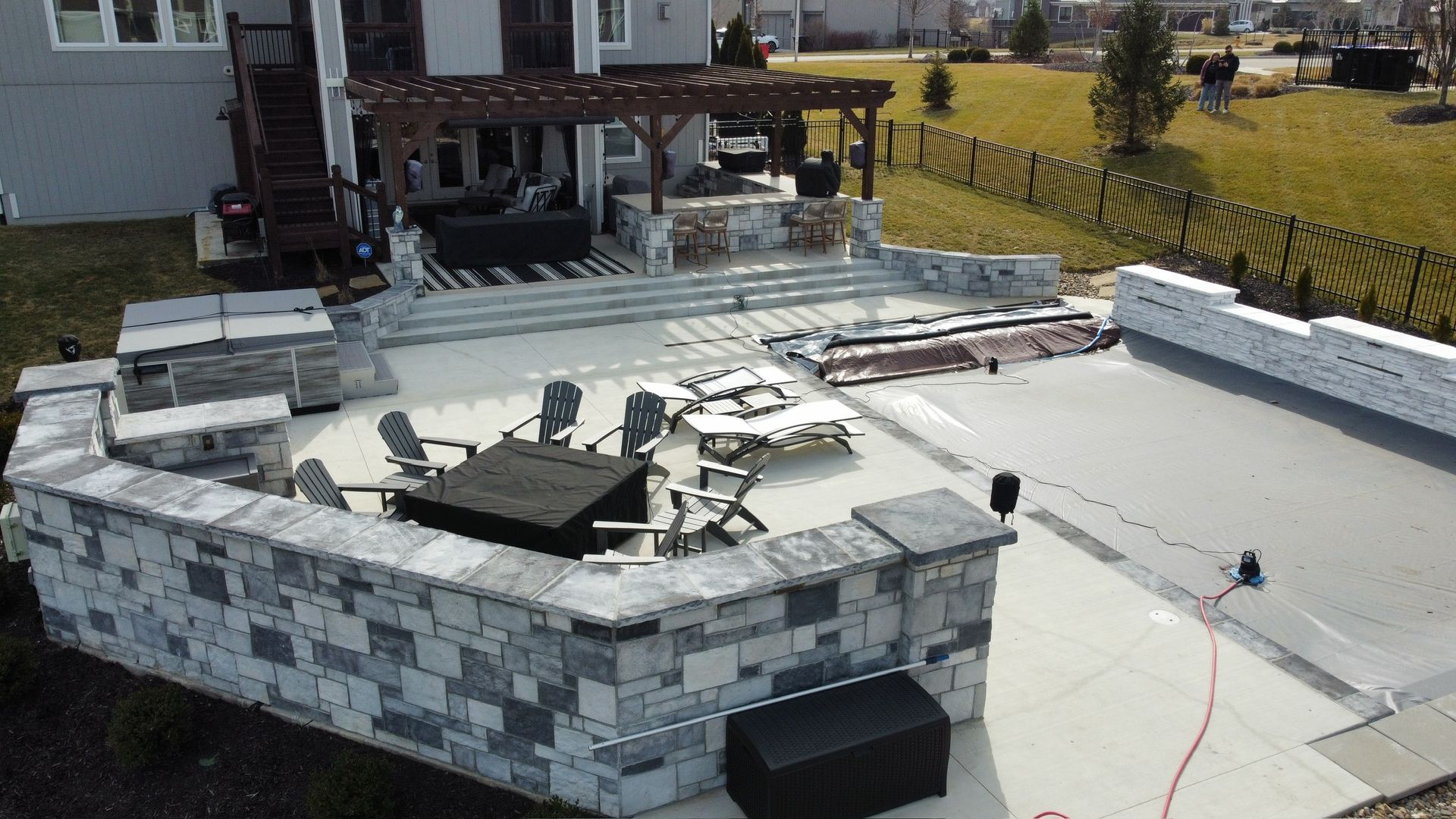 Stone patio and retaining walls under construction beside a house, with tools and materials on a sunny day