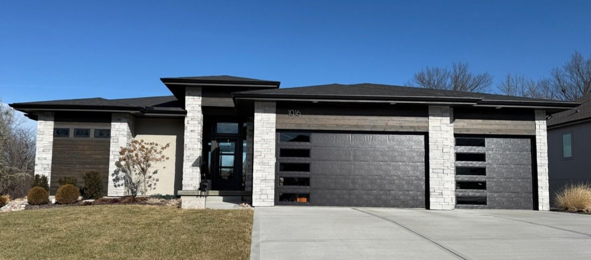Modern single-story house with a three-car garage and concrete driveway under a clear blue sky