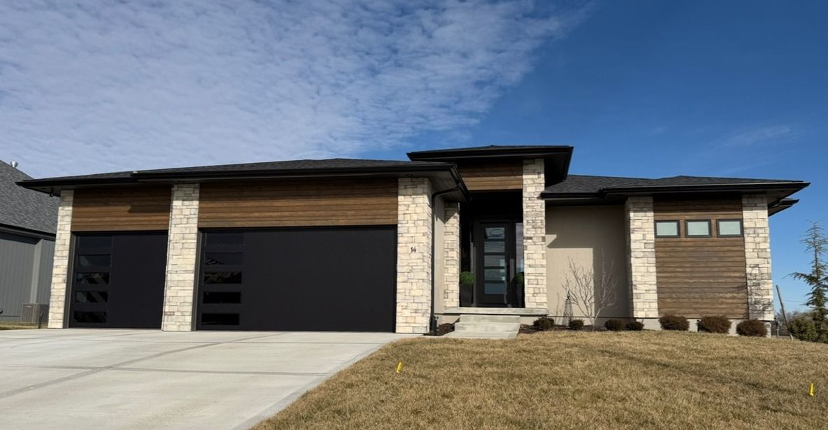 Modern single-story house with stone accents, three garage doors, and a sloped front lawn.