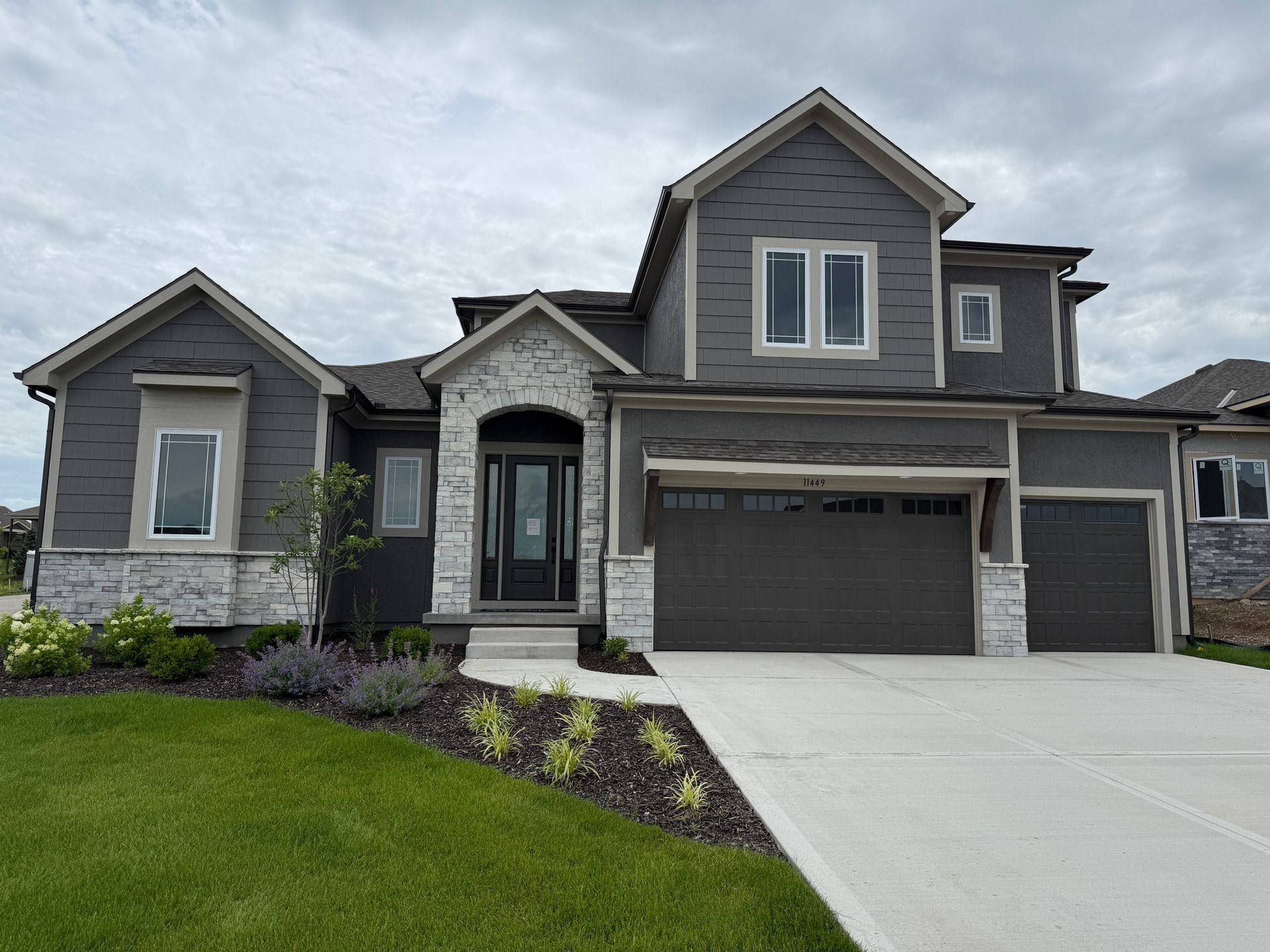Gray two-story suburban house with a three-car garage and a manicured lawn