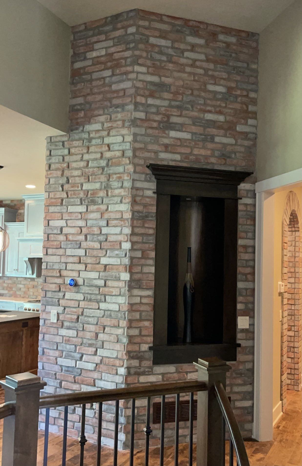 Tall brick fireplace wall in a home interior, beside a staircase railing and doorway.