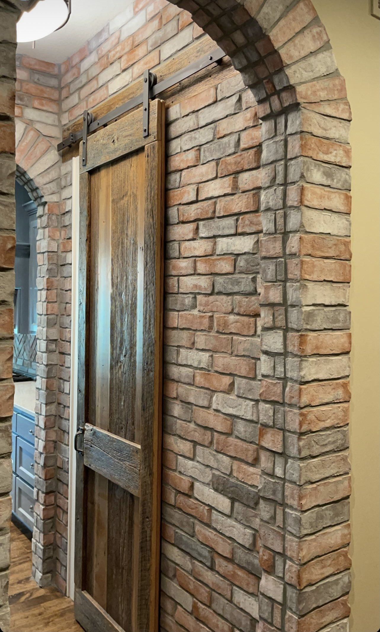Brick archway framing a weathered wooden door beside a glass entrance panel.