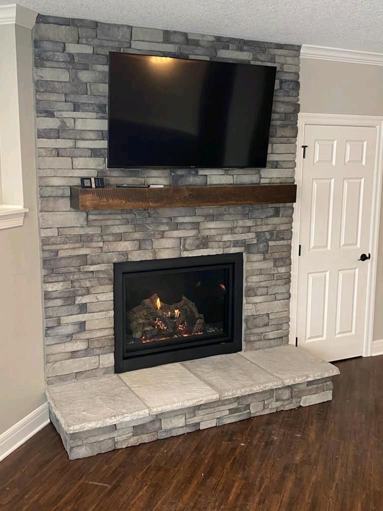 Stone fireplace with wall-mounted TV, electric insert, rustic mantel, and tiled hearth in a living room