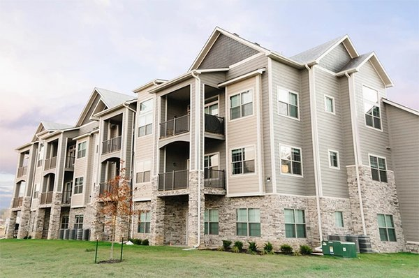Multi-story beige apartment building with stone accents and gabled roofs on a grassy lawn