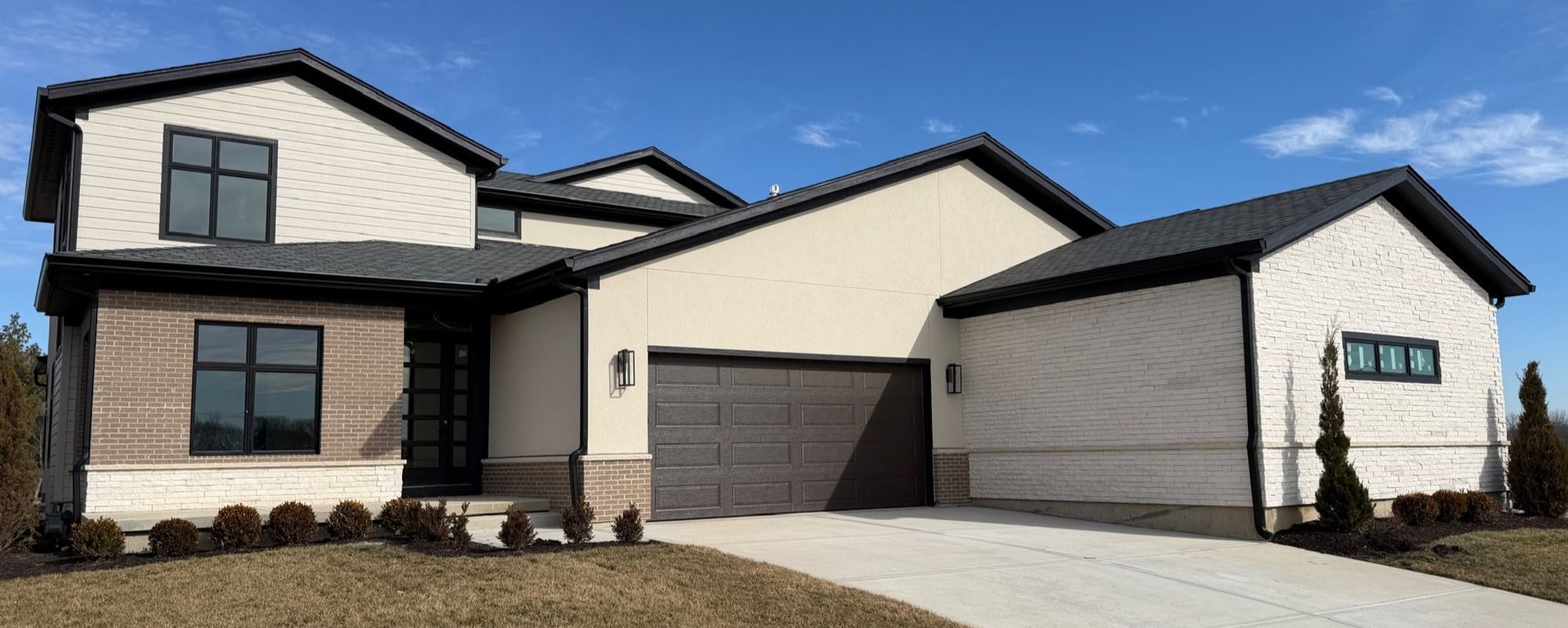 Modern two-story house with beige siding, dark trim, and a two-car garage in front view